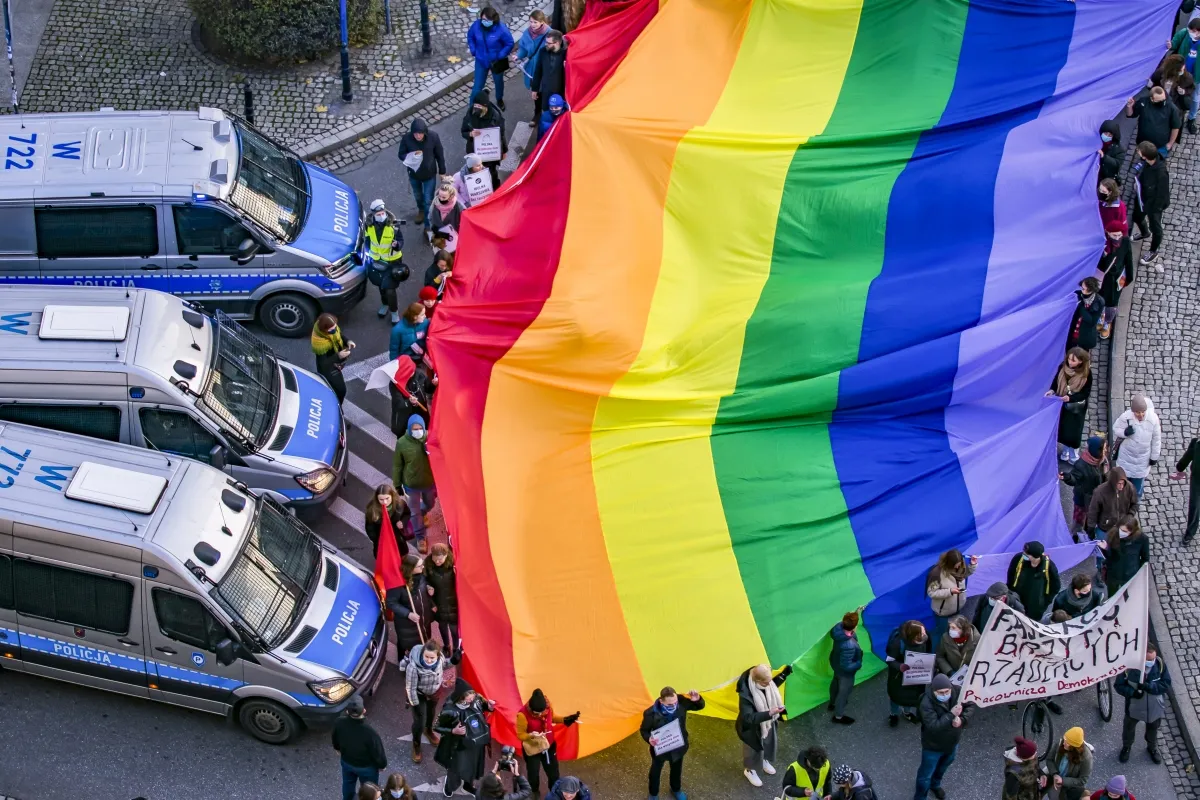 Huge rainbow flag seen from above beside a line of police vans